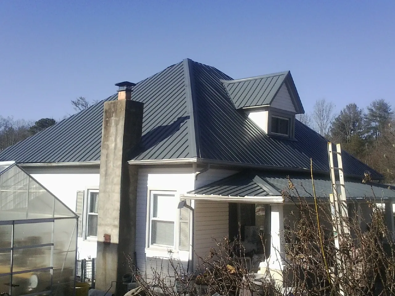 Dark blue standing seam metal roof on a white farmhouse with dormer — Slate & Tile Roof Repair by Roofing Brothers in Center Cross