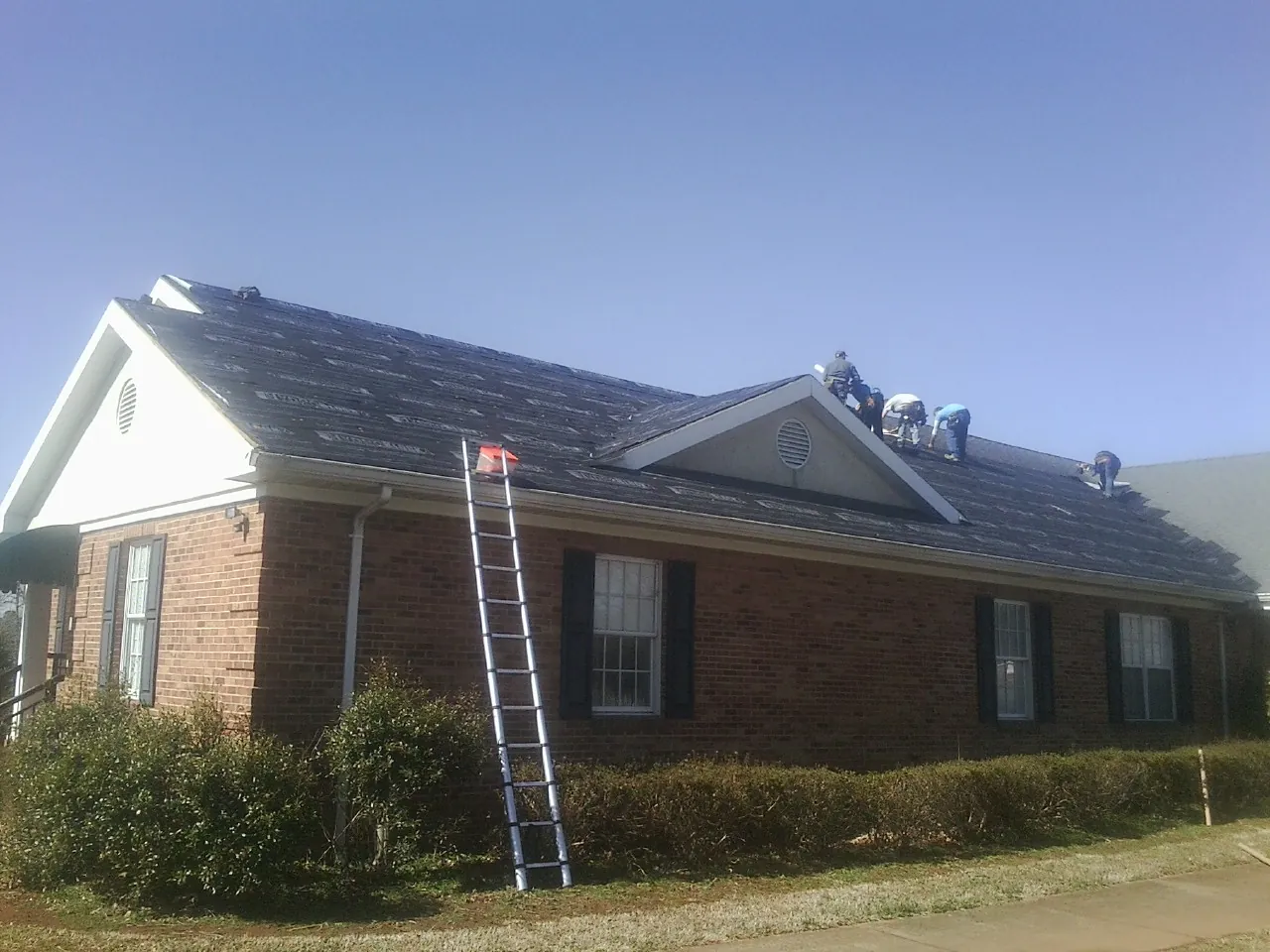 Crew tearing shingles off a brick ranch roof with a ladder set — Metal Roof Repair work by our crew in Center Cross