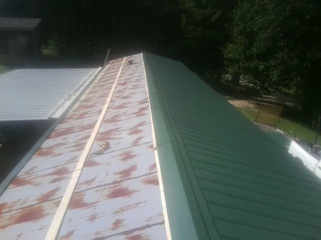 Old rusted panels beside newly installed green metal roofing — Wind Damage Roof Repair by Roofing Brothers in Center Cross