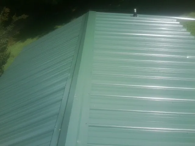 New green metal panels meeting at the ridge of a roof — Flat Roof Repair work by our crew in Center Cross