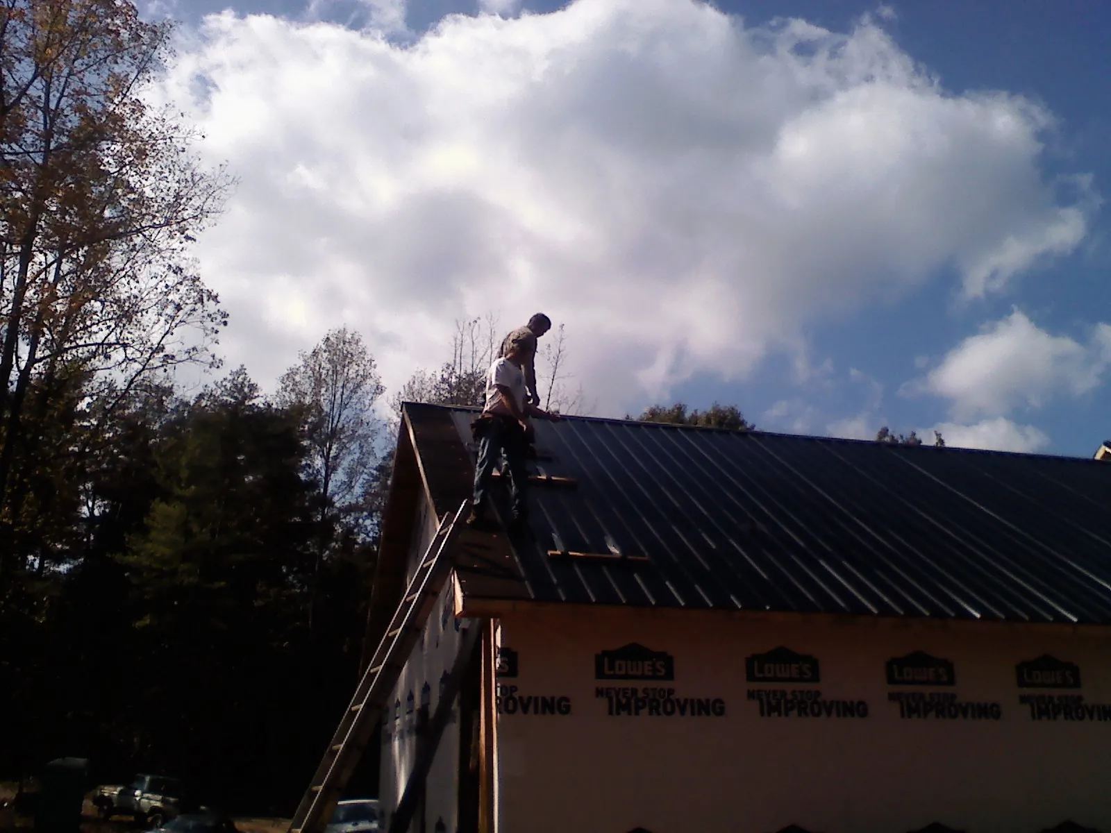 Roofer fastening dark metal panels high against a cloudy sky, from a Roof Inspection job in Center Cross