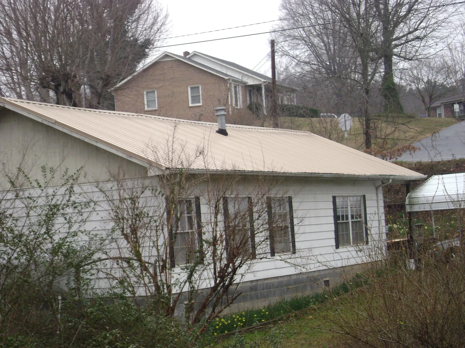 Tan metal roof on a white sided house set into a hillside — Commercial Roofing by Roofing Brothers in Center Cross