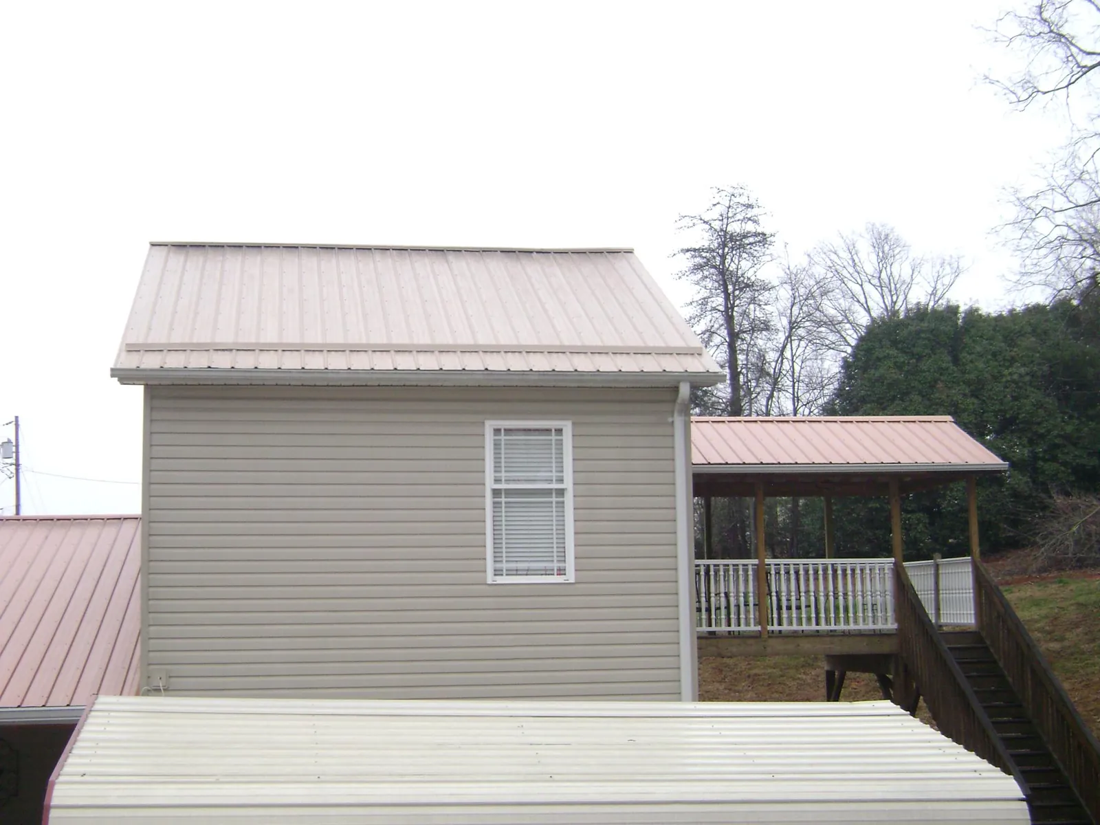 Tan metal roofs on a two story addition and attached porch, from a Roof Replacement job in Center Cross