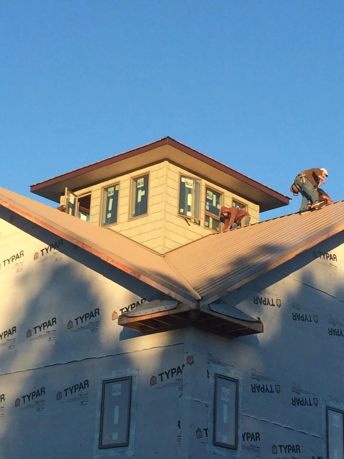 Roofers working around a rooftop cupola on a new metal roof at sunset — Roof Waterproofing in Center Cross by Roofing Brothers